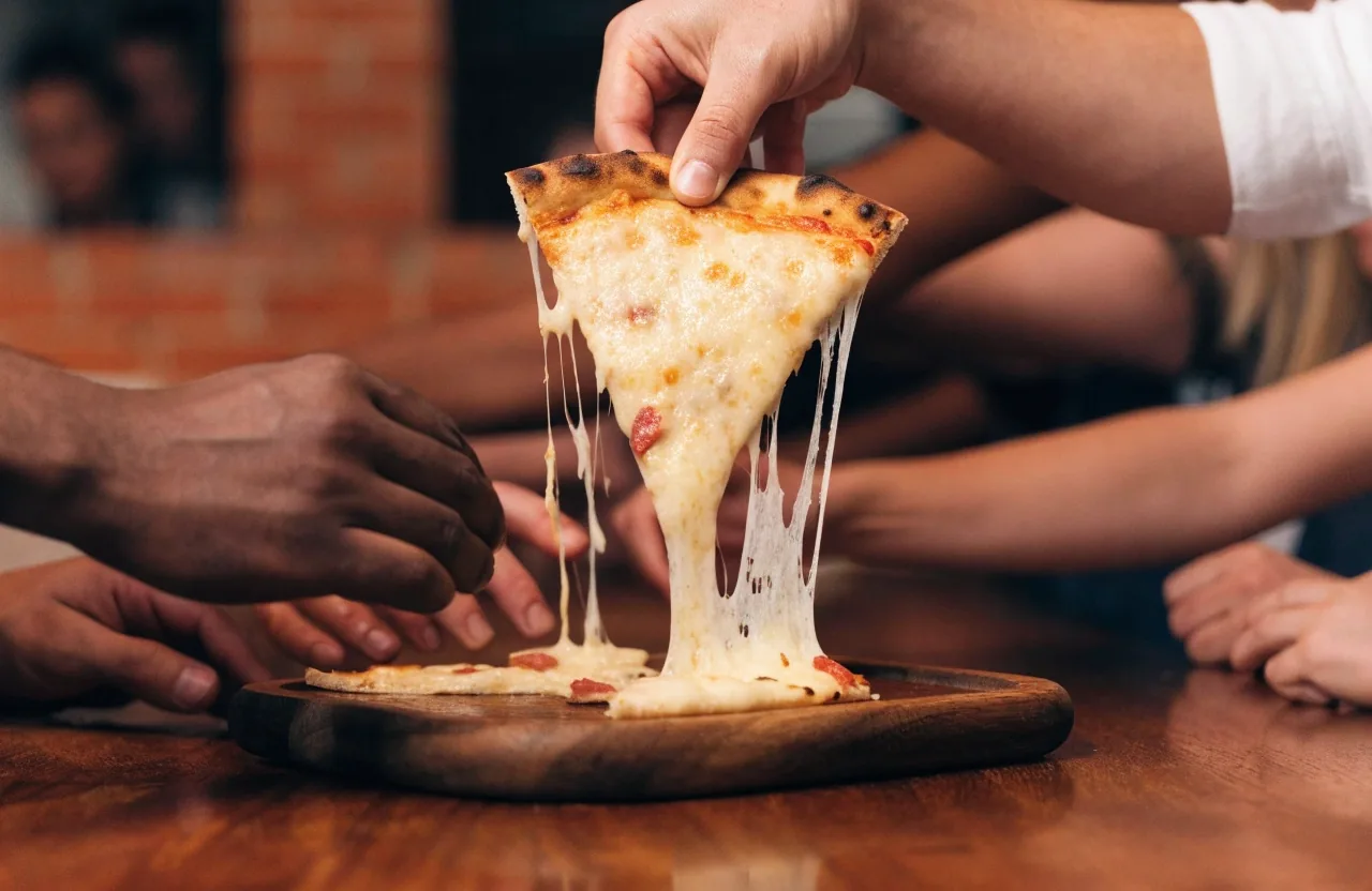 Hand lifting a hot slice of thin-crust pizza