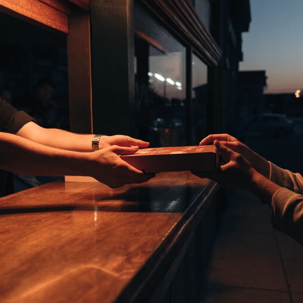 Counter-service window at dusk with a pizza box handoff